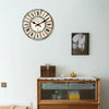 A rustic wooden wall clock with Roman numerals and a face showing Paris, mounted above a wooden cabinet.