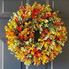 A circular wreath made of artificial flowers in shades of orange, yellow, and green hanging on a door.