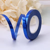 A roll of blue satin balloon ribbon lying on a white surface next to white flowers.