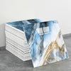 A stack of self-adhesive marble tile stickers featuring blue and gold veining on a gray background.