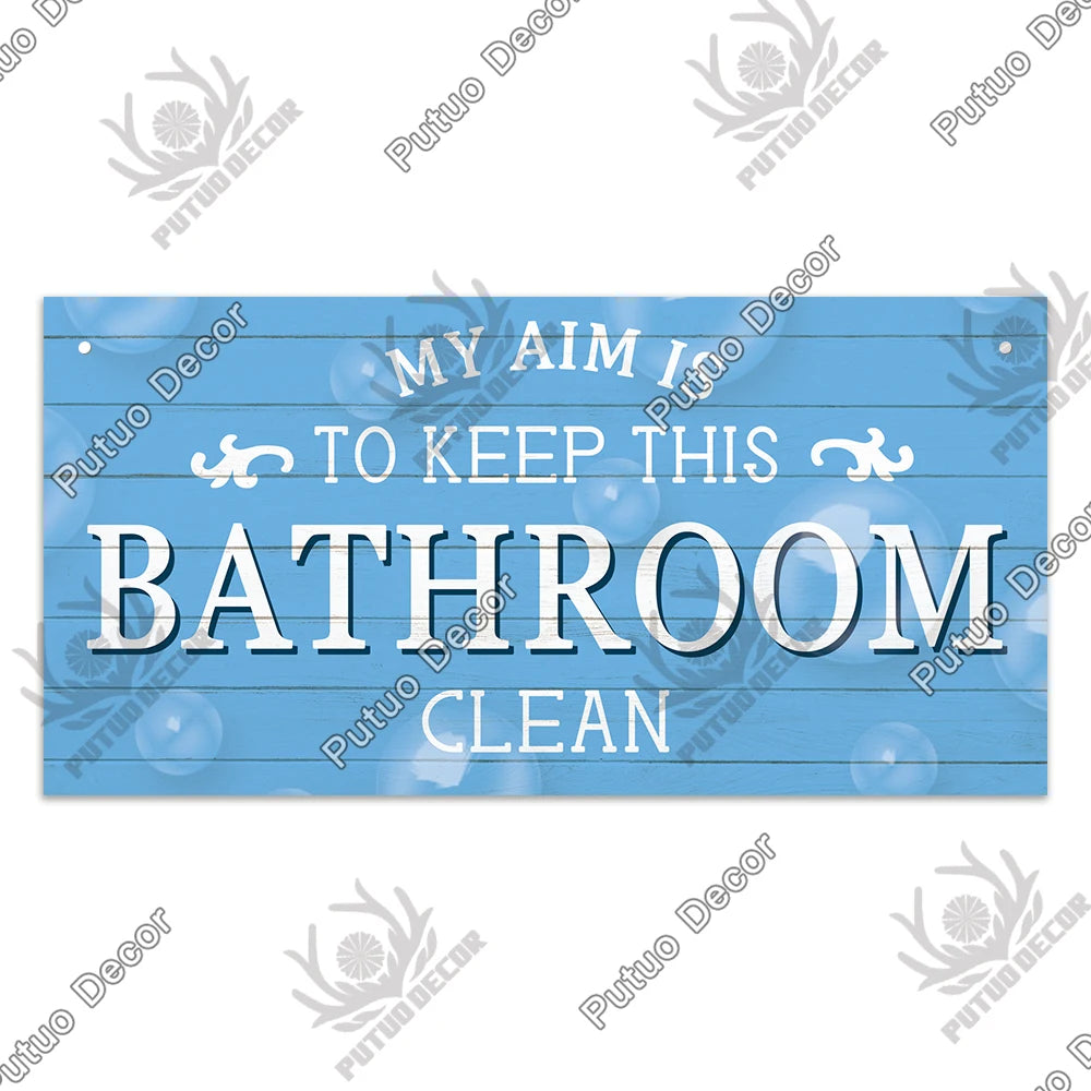 A light blue wooden sign with white text that reads My aim is to keep this bathroom clean.