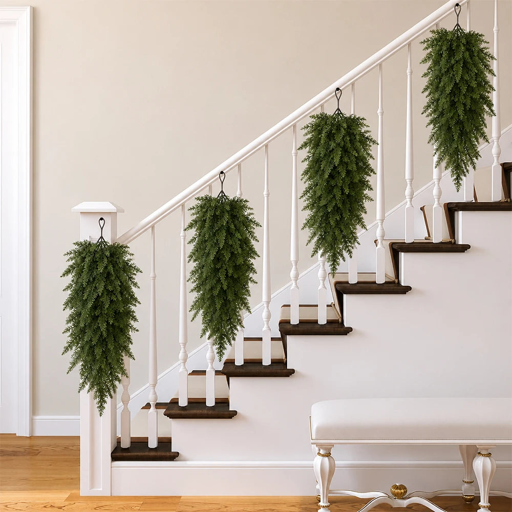 A white staircase railing decorated with green artificial Christmas teardrop swag featuring Norfolk pine needles.