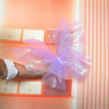 A hand holds a translucent purple silk artificial butterfly decoration against an orange-lit background.