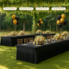 A long black stretch rectangle tablecloth set up outdoors for a family gathering or picnic with floral decorations and balloo