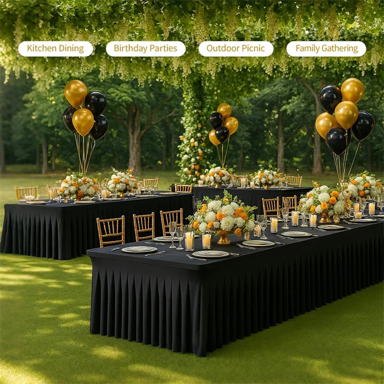 A long black stretch rectangle tablecloth set up outdoors for a family gathering or picnic with floral decorations and balloo