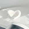 White resin sculpture shaped like a heart with delicate angel wings resting on a piece of white paper.