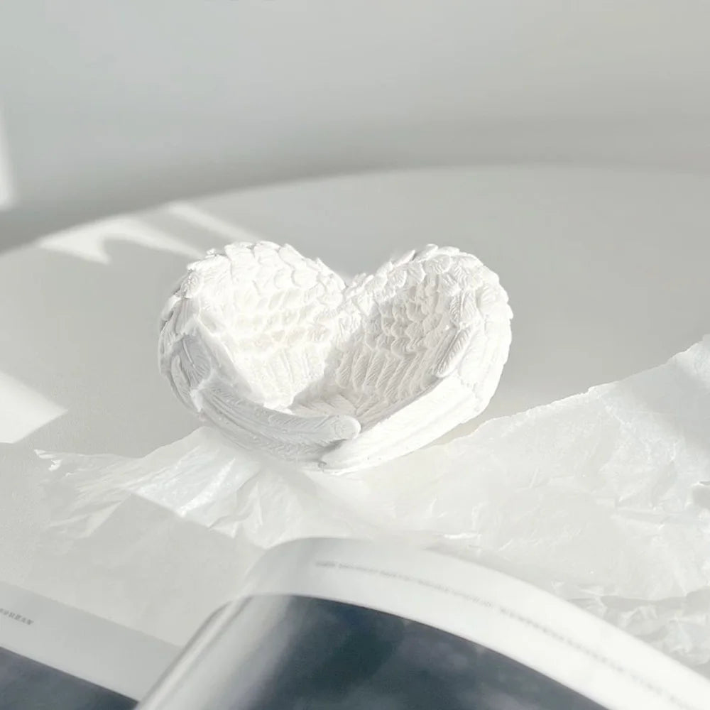 White resin sculpture shaped like a heart with delicate angel wings resting on a piece of white paper.