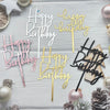 A set of elegant black and gold acrylic cake toppers for birthday parties displayed on a light wooden surface.