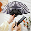 A hand is opening a black and white vintage silk bamboo folding hand fan.