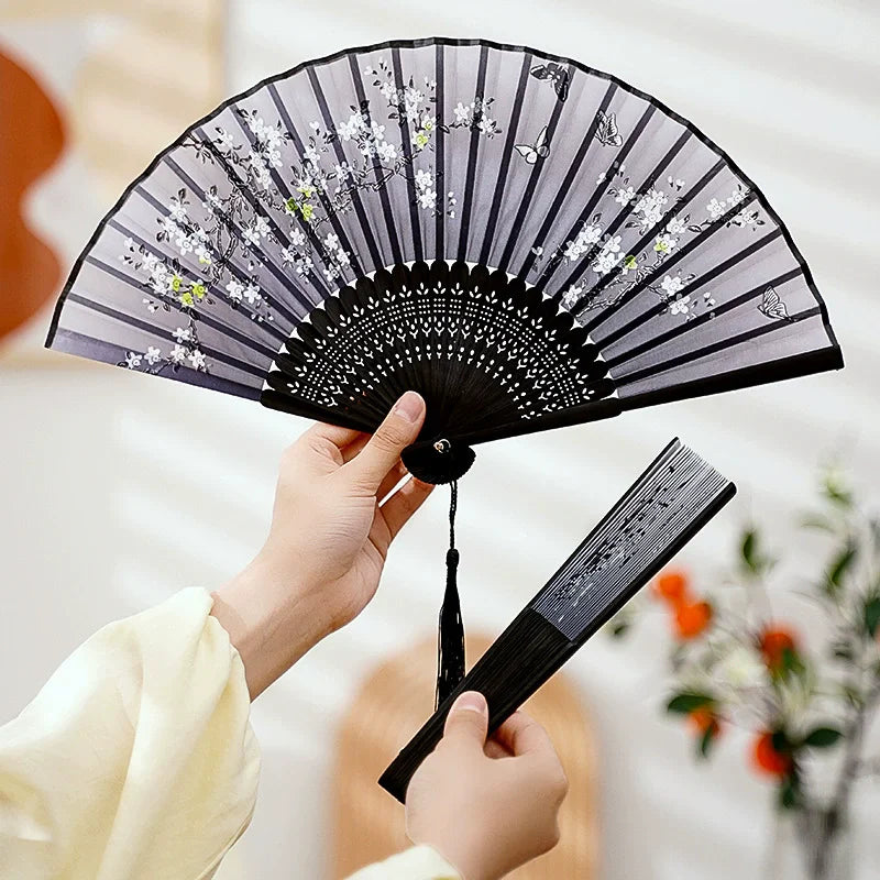 A hand is opening a black and white vintage silk bamboo folding hand fan.