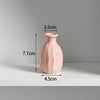 A pink ceramic mini vase with a rounded body and narrow neck, shown against a light gray background.