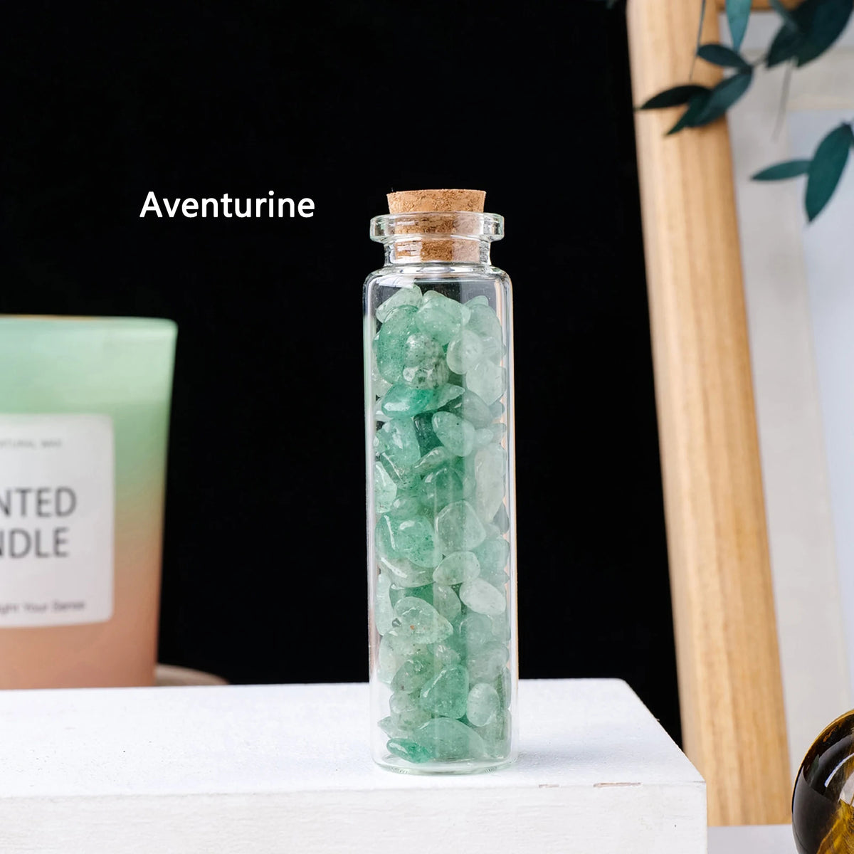 A clear glass bottle filled with green aventurine crystals sits on a white surface.