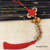 Red silk tassel featuring an antique copper five emperor coin pendant tied with a Chinese knot on beige fabric.