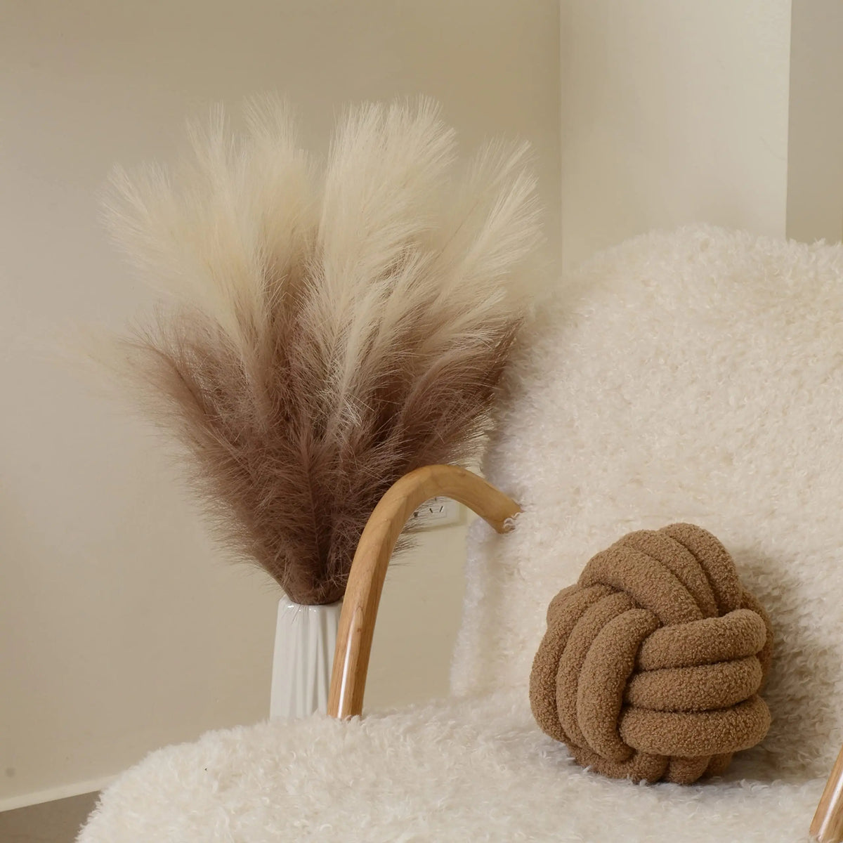 Dried pampas grass branches in shades of beige and brown displayed on a white surface.
