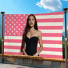A woman posing in front of a large American flag tapestry featuring red, white, and pink stripes and stars.