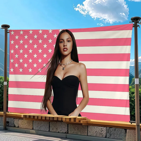 A woman posing in front of a large American flag tapestry featuring red, white, and pink stripes and stars.