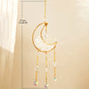 A gold moon-shaped crystal suncatcher with dangling rainbow prisms suspended by a chain.