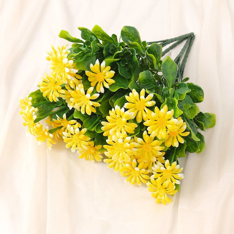 A bouquet of yellow and white daisies with green foliage arranged on a light-colored fabric.