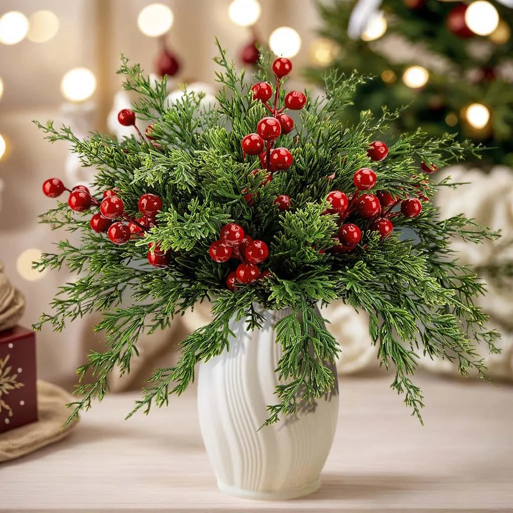 A bouquet of artificial Christmas berry stems and pine branches in a white vase on a wooden surface.