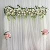 A floral garland of white roses and greenery draped across a sheer white curtain backdrop for event decor.
