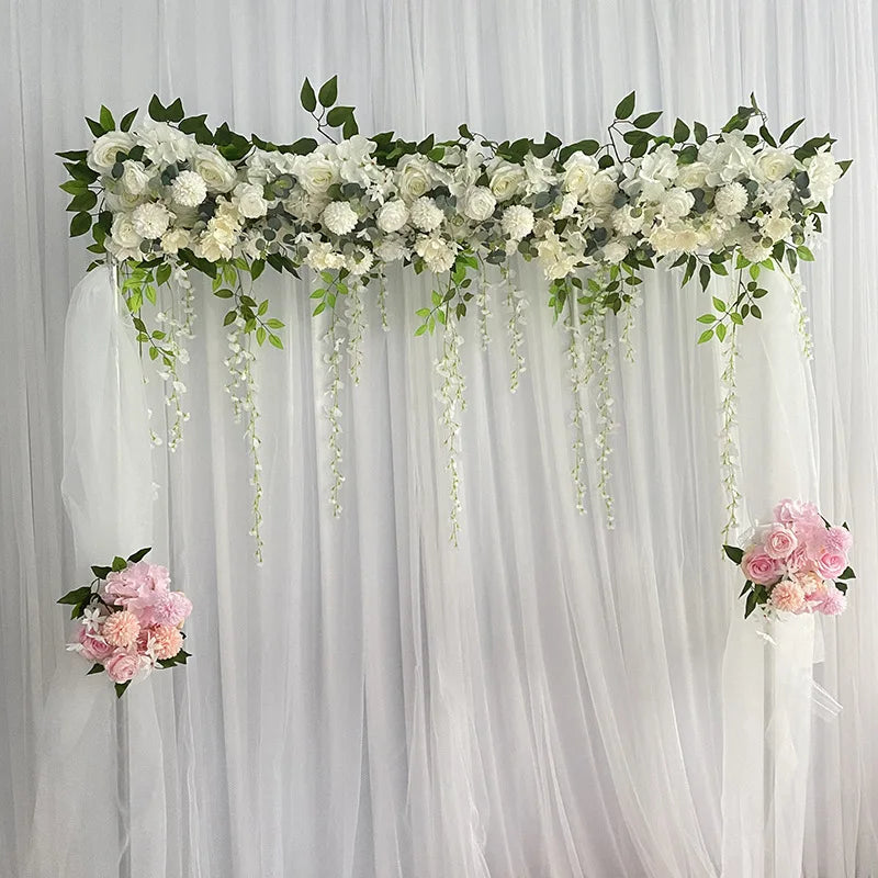 A floral garland of white roses and greenery draped across a sheer white curtain backdrop for event decor.