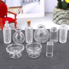 A set of clear glass containers including a bottle, various small vessels, and a bowl for a miniature dollhouse display.