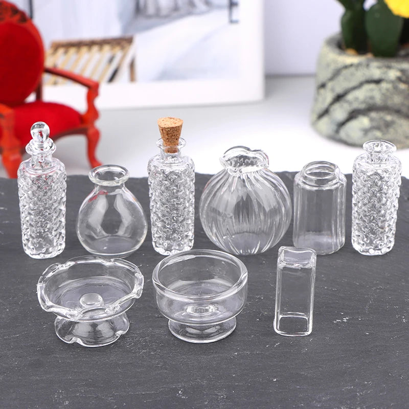 A set of clear glass containers including a bottle, various small vessels, and a bowl for a miniature dollhouse display.