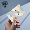 A hand holds a holographic cat credit card skin sticker displaying a cat face design.