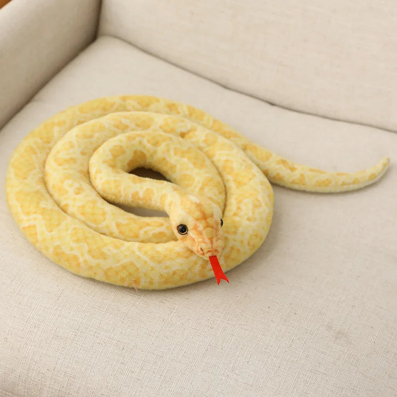 A yellow giant realistic snake plush toy resembling a boa coiled on a light fabric surface.