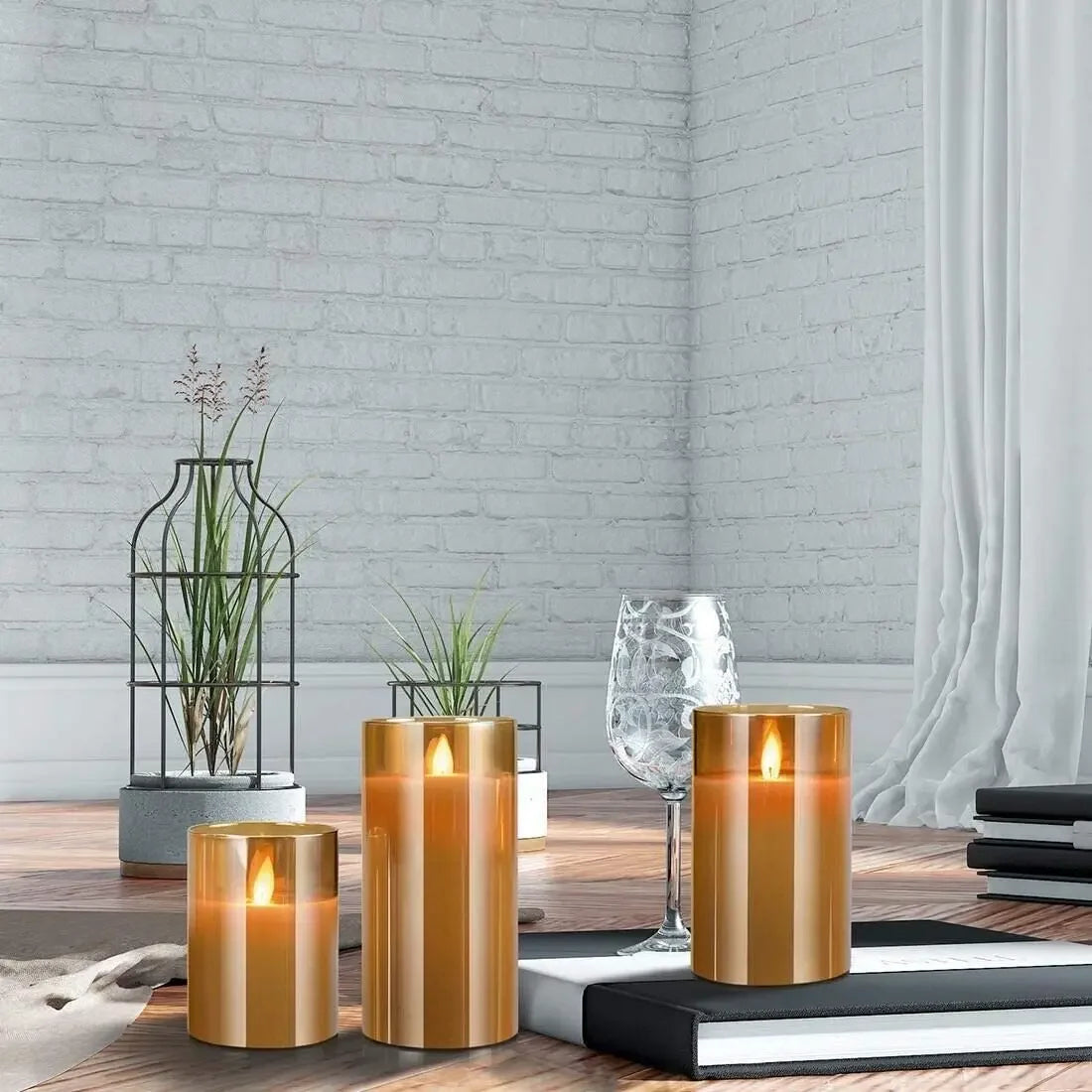 Three glass pillar candles in gold and amber tones resting on a wooden surface with stacked books.