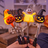Une main tient quatre lanternes d'Halloween orange et jaunes lumineuses avec des visages sculptés, sur un arrière-plan flou.