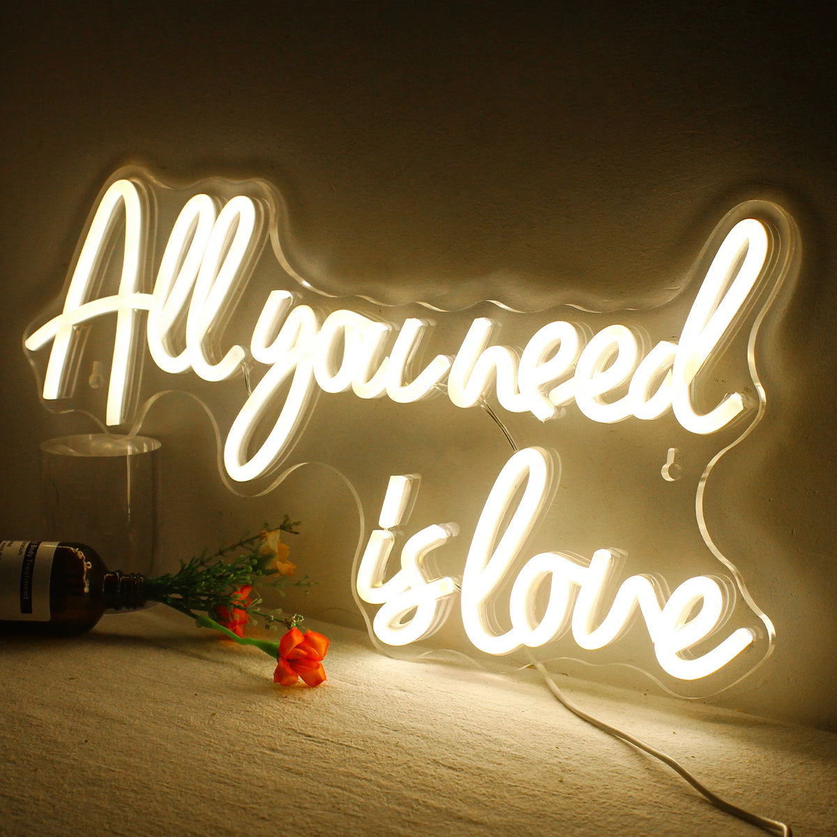 A glowing neon sign spelling out All you need is love on a wall with a wooden surface.