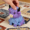 A hand is holding a purple Scottish Highland Cow squishy stress relief toy on a light-colored rug.