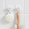White adjustable self-adhesive curtain rod brackets mounted on a white tiled wall with a wooden shower brush hanging below.