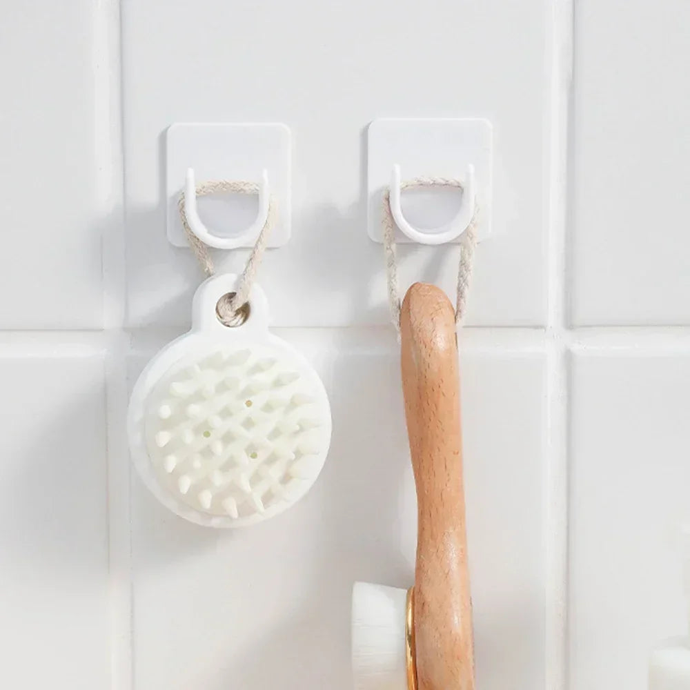 White adjustable self-adhesive curtain rod brackets mounted on a white tiled wall with a wooden shower brush hanging below.
