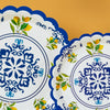 White disposable paper plates with blue floral and lemon designs on a beige background.