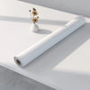 A roll of matte peel and stick decor stickers lying on a white surface next to a small vase with dried flowers.