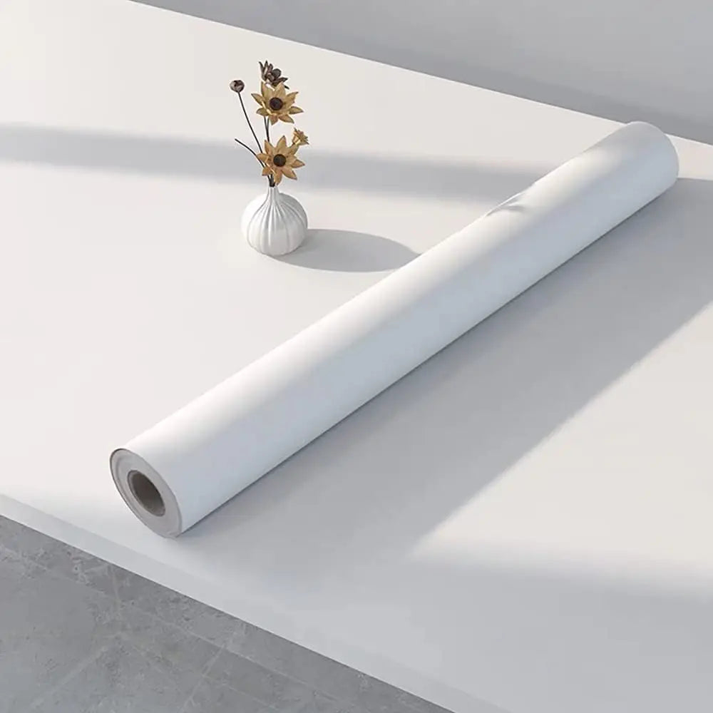 A roll of matte peel and stick decor stickers lying on a white surface next to a small vase with dried flowers.