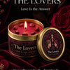 A jar of The Lovers Tarot candle in gold packaging with a red wax, set against a dark background and red roses.