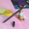 A black calligraphy pen with a gold tip rests on a pink surface next to a small stuffed animal and citrus slices.