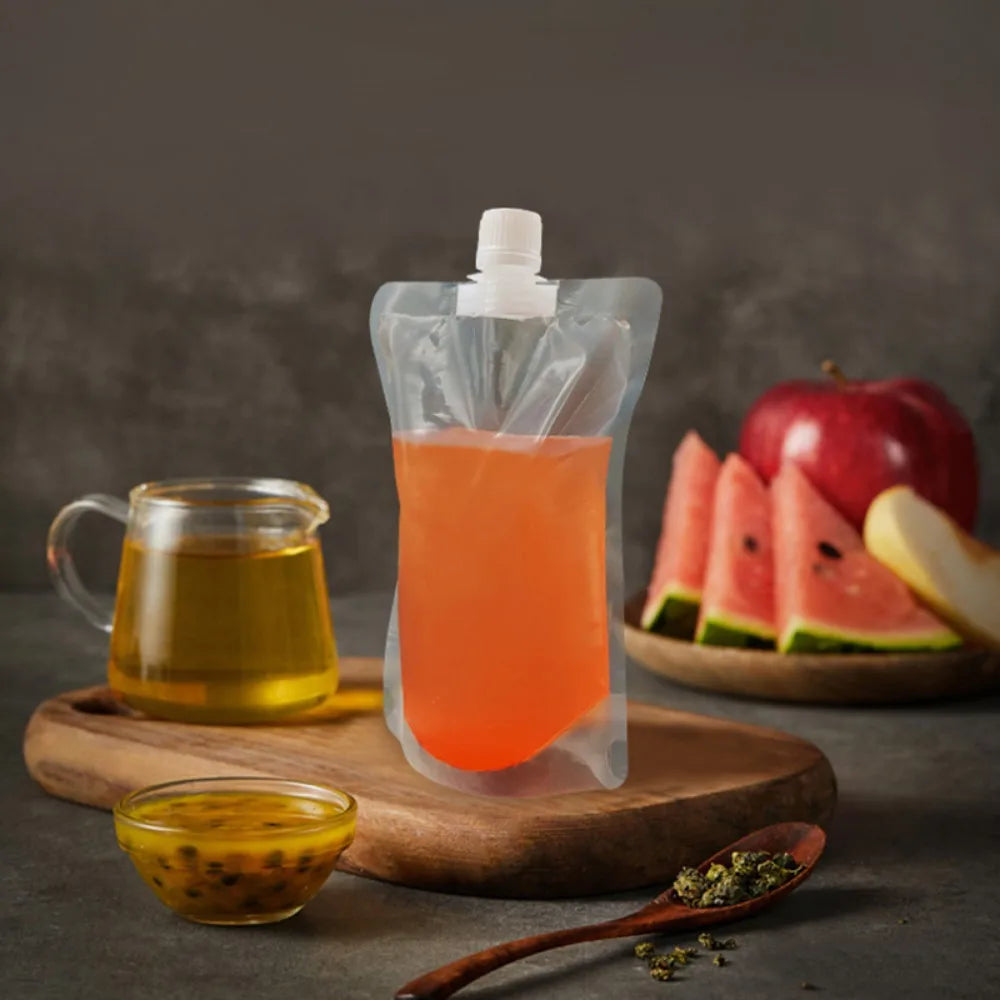 A clear liquid drink is contained in a resealable pouch on a wooden board with a glass jug and a slice of watermelon.