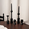 A set of two black candle holders with tall, fluted candles displayed on a dark wooden table.