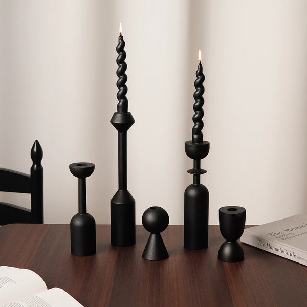 A set of two black candle holders with tall, fluted candles displayed on a dark wooden table.