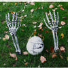 A pair of realistic white skeleton arm stakes lying on green grass with fallen autumn leaves.
