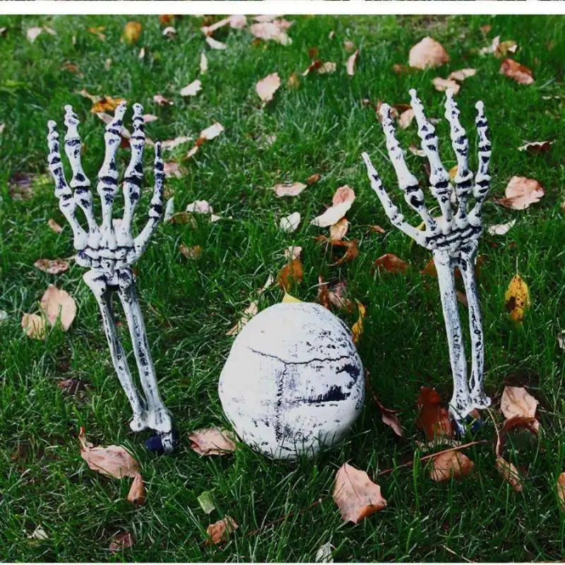 A pair of realistic white skeleton arm stakes lying on green grass with fallen autumn leaves.