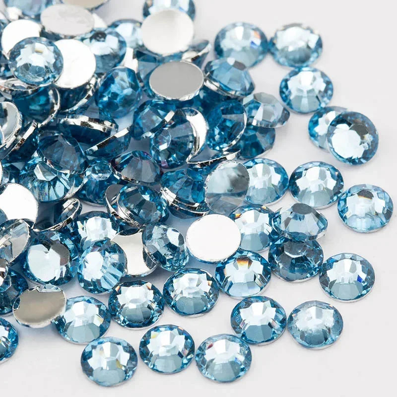 A pile of round, flatback resin rhinestones in various shades of blue and clear glass on a white background.