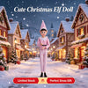 A cute Christmas elf doll dressed in pink striped pajamas standing in a snowy village setting.