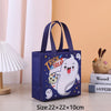 A dark blue non-woven gift tote bag with a white ghost design and stars, shown on a wooden surface.