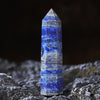 A tall, pointed blue lapis lazuli crystal tower resting on a dark, textured surface.