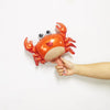 An orange foil balloon shaped like a crab is being held by a hand against a white background.